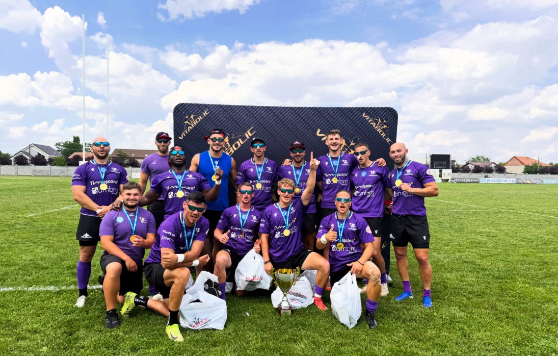 Rugby team in purple jerseys posing on a sunny field with medals and a trophy after winning.