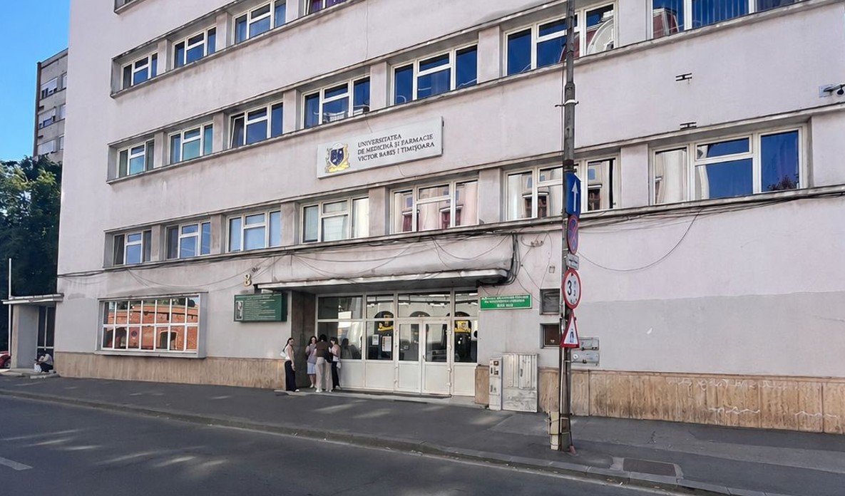 Front view of a white multi-story medical university building with people gathered at the entrance on a city street.