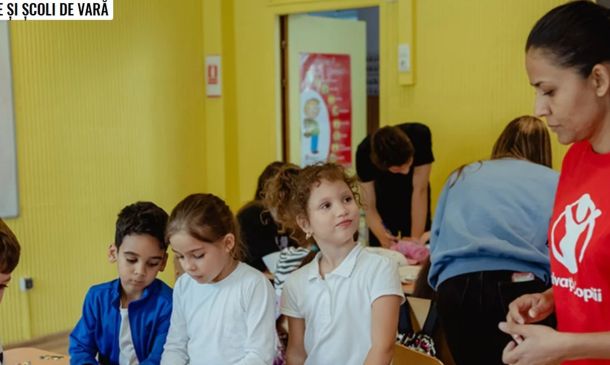 Children participate in a summer camp activity in a yellow classroom; a staff member in a red shirt supervises.