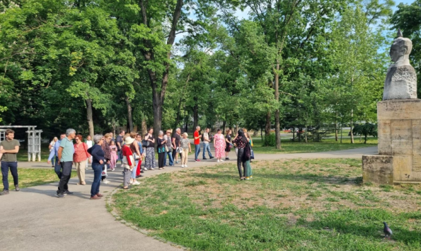 Tour group gathered in a sunny park near a stone statue on a pedestal.