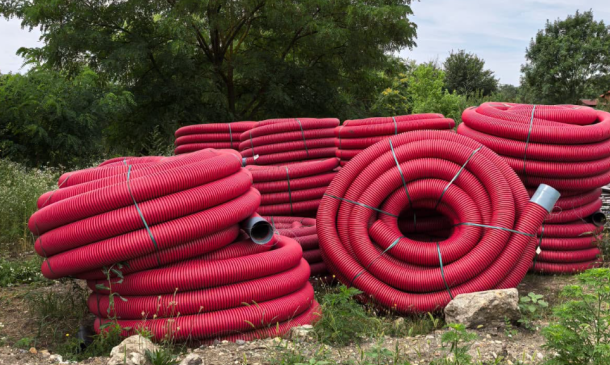 Stacks of large red coiled flexible plastic hoses outdoors on rocky ground.