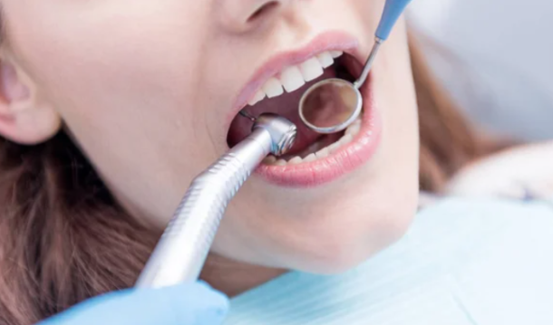 Close-up of a patient's mouth during a dental examination with a mirror and dental scaler in use.